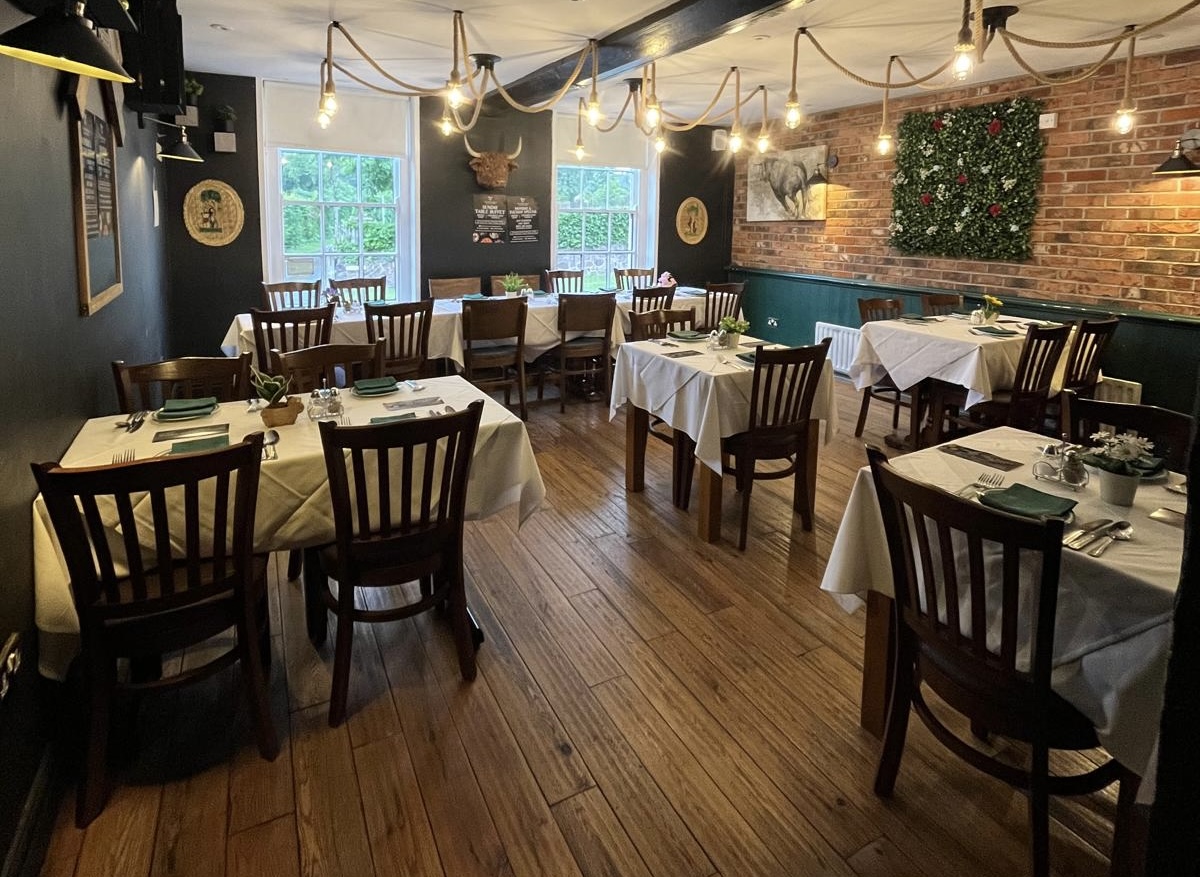 The dining room at The Bull's Head, set for service with warm rope lighting and garden views